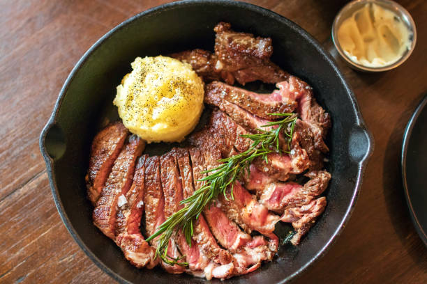 スライスしたリブアイの鋳鉄板は、テーブルの上にソースでマッシュポテトとソースとミディアムレアステーキを調理します。 - rib eye steak steak beef prepared potato ストックフォトと画像
