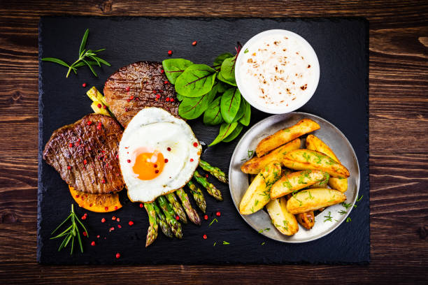 grilled steak with sunny side up egg, fried potatoes and vegetable salad - red meat meat dish grilled rare imagens e fotografias de stock