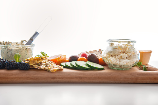 Vegan boursin, feta and cheddar cheese in recycled jars.  Raw fruit, berries, vegetables, whole grain bread and crackers on reclaimed wood serving board.