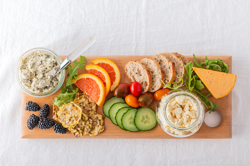 Personal perspective.  Vegan boursin, feta and cheddar cheese in recycled jars.  Raw fruit, berries, vegetables, whole grain bread and crackers on reclaimed wood serving board.