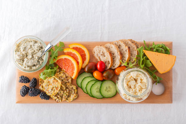 Healthy Vegan Cheese, Fruit, Vegetable, Crackers, Bread on Recycled Board Personal perspective.  Vegan boursin, feta and cheddar cheese in recycled jars.  Raw fruit, berries, vegetables, whole grain bread and crackers on reclaimed wood serving board. spread food stock pictures, royalty-free photos & images