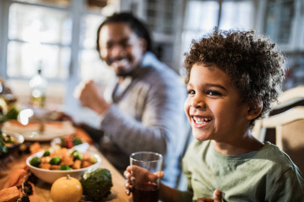 istock Cute happy black boy having a meal at dining table. 1164867725