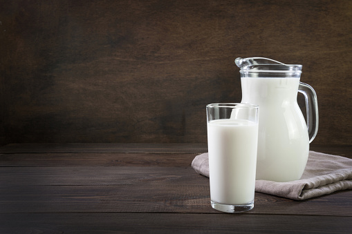 Fresh milk in glass and pitcher on dark wooden table. Healthy vegan eating. Rustic style.