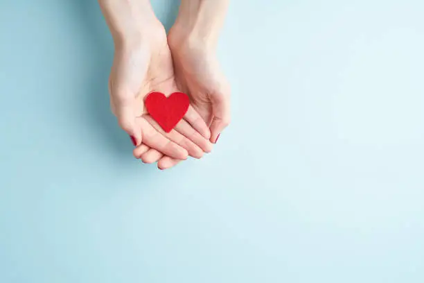 Photo of a person holding red heart in hands, donate and family insurance concept, on aquamarine background, copy space top view