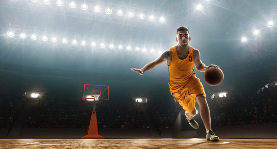 Young muscular basketball player with a ball on floodlight professional court scoring a goal