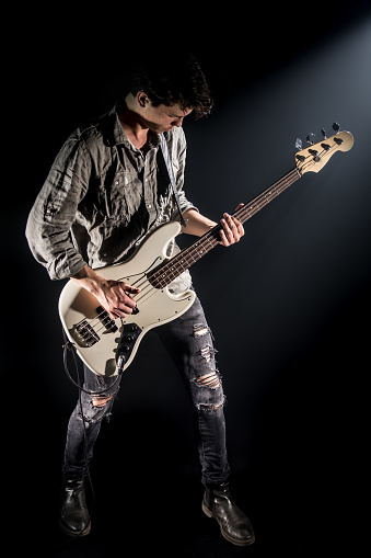 the musician plays bass guitar, on a black background with a beam of light, emotional play, music concept