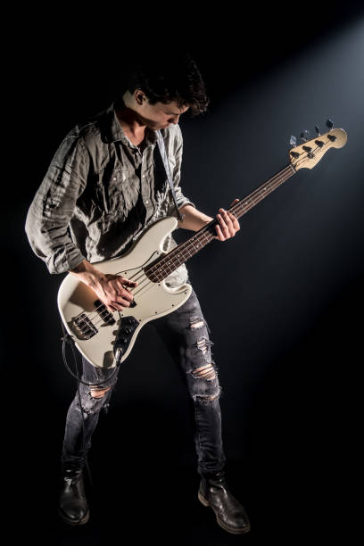 o músico joga a guitarra baixa, em um fundo preto com um feixe de luz - rock bass - fotografias e filmes do acervo