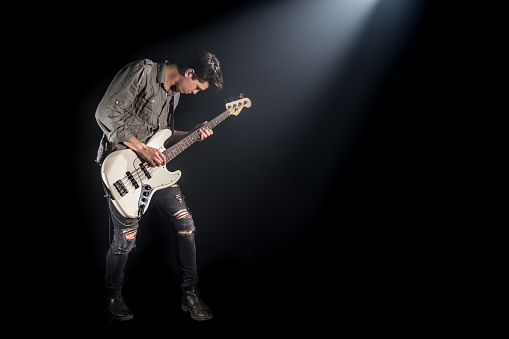 the musician plays bass guitar, on a black background with a beam of light, emotional play, music concept