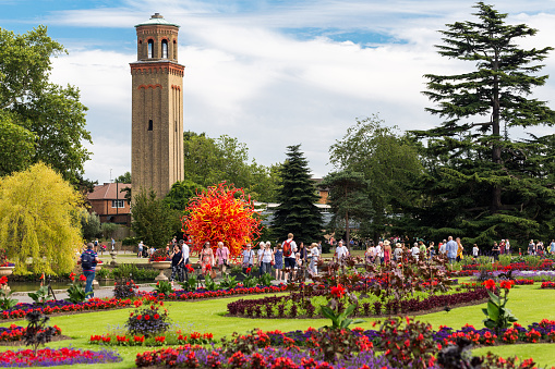 Kew, UK - 5 July, 2019: color image depicting crowds of people wandering around the brightly-colored flower beds and lush green manicured lawns of Kew Gardens, just outside of the city of London, UK.