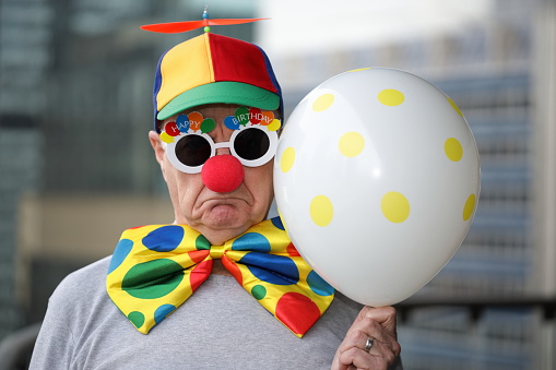 Smiling funny clown with a multi colored wig holding a blank white sign. Isolated on white. You can add extra white space with your message to the bottom.