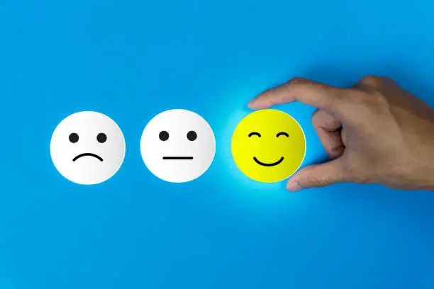 Photo of Conceptual the customer responded to the survey. The client using hand choose happy face smile icon on blue background.Depicts that customer is very satisfied. Service experience satisfaction concept.