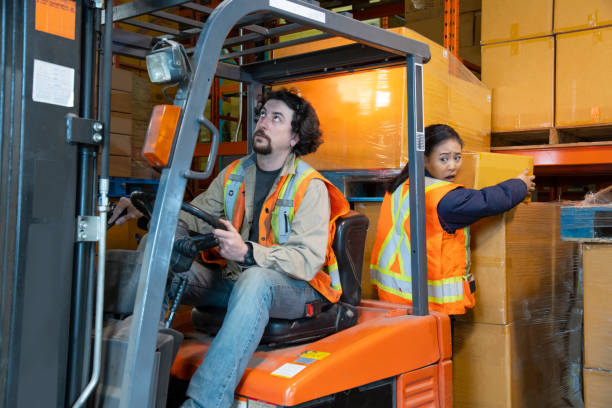 an industrial warehouse workplace safety topic. a worker in the danger zone, working behind a forklift carrying a load. - wrong injury imagens e fotografias de stock