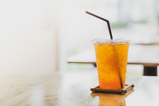 Iced lemon tea in plastic cup with brown plastic straw with blured cafe background.