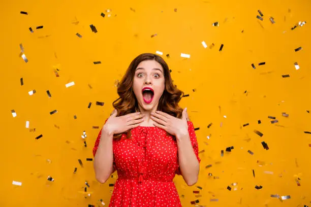 Pretty lady surprised by unexpected, birthday party arranging wear red dress isolated yellow background