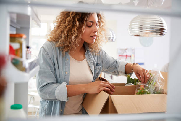 vista mirando desde el interior del refrigerador como mujer desempaqueta la entrega de alimentos en el hogar en línea - green box fotografías e imágenes de stock