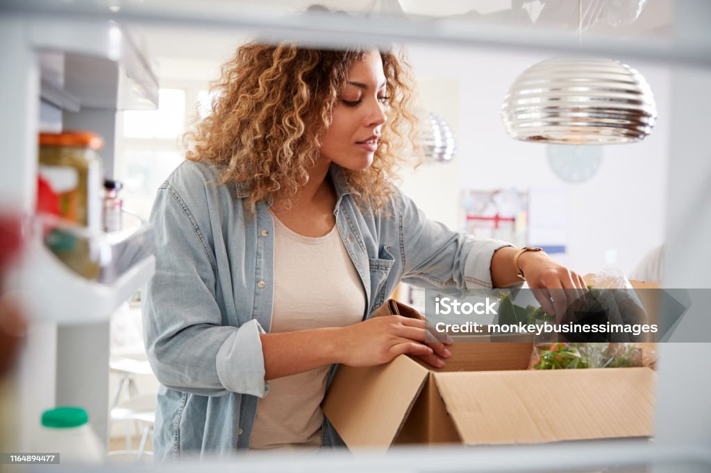 女性がオンラインホームフード配達を解凍するように冷蔵庫の中から外を見る - 配達のロイヤリティフリーストックフォト