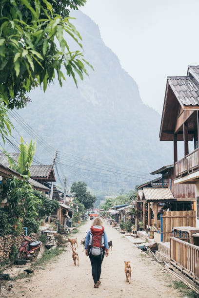 young caucasian blonde woman with backpack walking on the central street of muang ngoi village, laos - dirtroad imagens e fotografias de stock