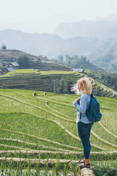 Young Caucasian blonde woman in denim shirt overlooking Sapa rice terraces at sunset in Lao Cai province, Vietnam stock photo