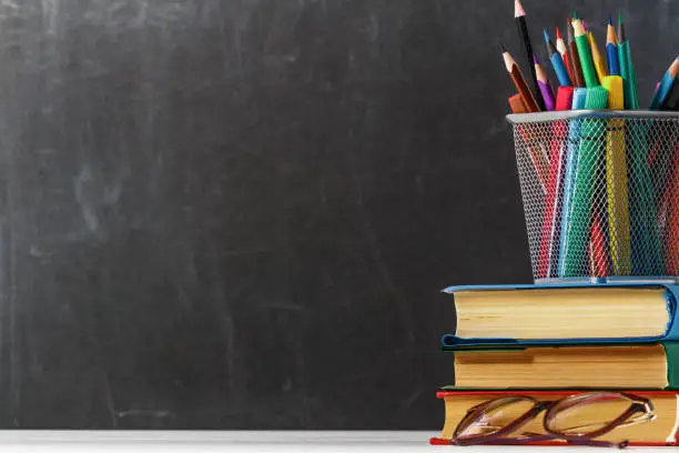 Photo of A stack of books, glasses, pencils on the background of a black school board. The concept of education. Copy space.