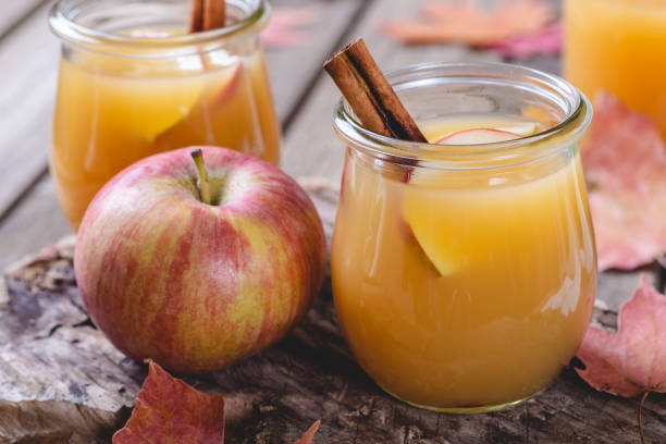 Glass of Apple Cider Closeup of a glass of apple cider with sliced apples and cinnamon stick next to an apple on a rustic wooden surface apple juice photos stock pictures, royalty-free photos & images