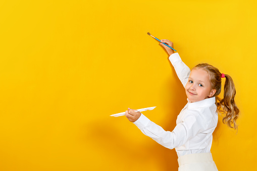 Little girl holding a palette and brush. A child is painting on a yellow empty wall.