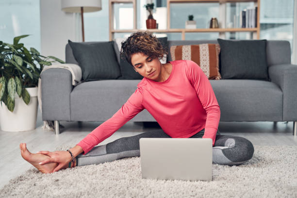 Multitasking is the easiest thing I've ever done Full length shot of an attractive young woman multitasking and using a laptop while stretching in her living room online yoga stock pictures, royalty-free photos & images