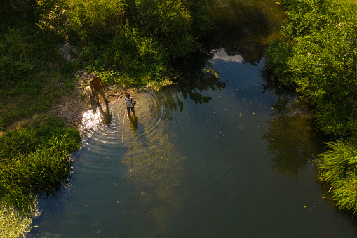 Drone point view of teenage boy and his dad fishing on the river in nature, having fun, dog is near them