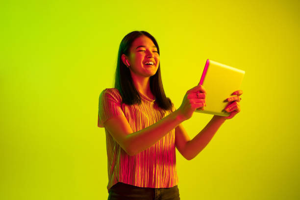 istock Beautiful girl's facial expression in neon light on yellow studio background 1164899708
