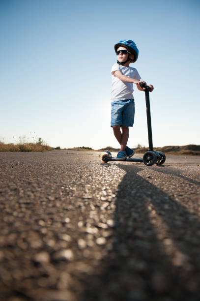 istock active little boy in helmet and sunglasses standing on asphalt empty highway with scooter in summer heat desert 1164899737