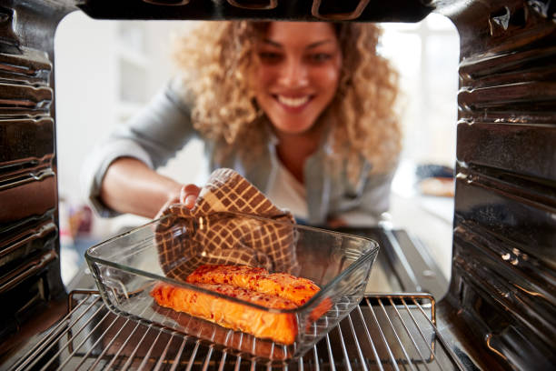 vista guardando fuori dal forno interno mentre donna cucina salmone al forno al forno - salmone frutto di mare foto e immagini stock