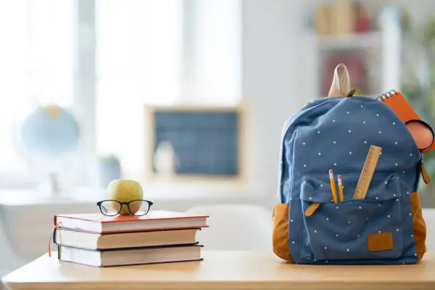 Back to school and happy time! Apple, pile of books and backpack on the desk at the elementary school.