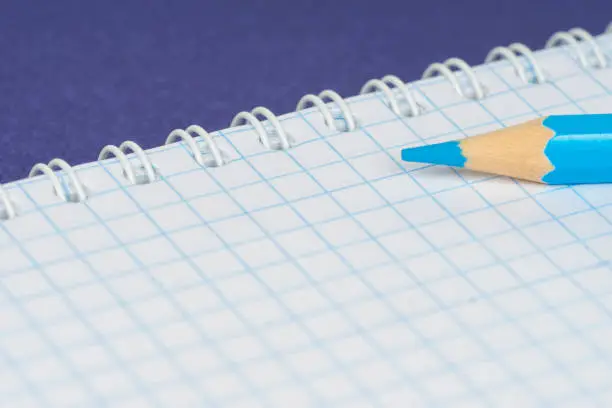 open spiral notebook with pencil on blue paper background