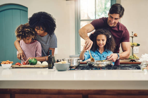 Families who cook together, enjoy their food even more Shot of a family of four cooking together in their kitchen at home chopping food photos stock pictures, royalty-free photos & images