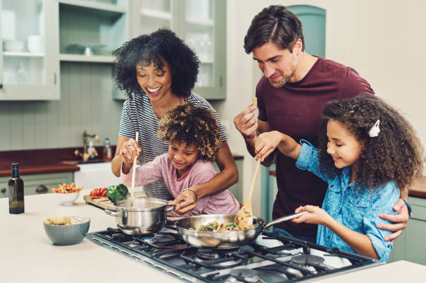 A meal cooked by the whole family tastes better Shot of a family of four cooking together in their kitchen at home stove stock pictures, royalty-free photos & images
