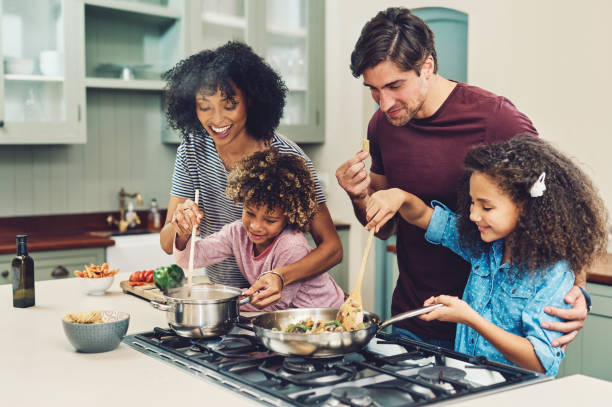 A meal cooked by the whole family tastes better Shot of a family of four cooking together in their kitchen at home family get together stock pictures, royalty-free photos & images