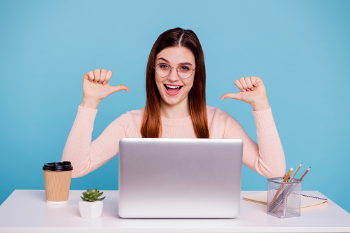 Close up photo beautiful she her lady hands arms fingers indicate direct herself advertising notebook coffee cup table desk wear specs casual pastel warm pullover isolated bright blue background