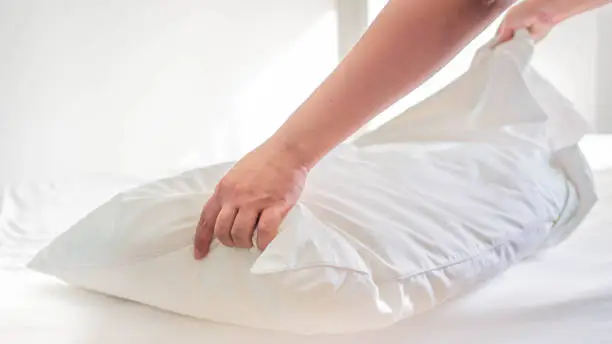 White pillow on the bed in the bedroom with woman 's hand who are making the room.