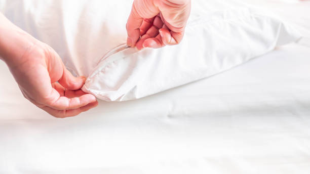 White pillow on the bed in the bedroom with woman 's hand who are making the room. stock photo