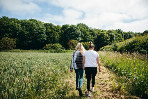 A rear-view shot of an lgbtqi couple walking through a field together, they are wearing casual clothing.