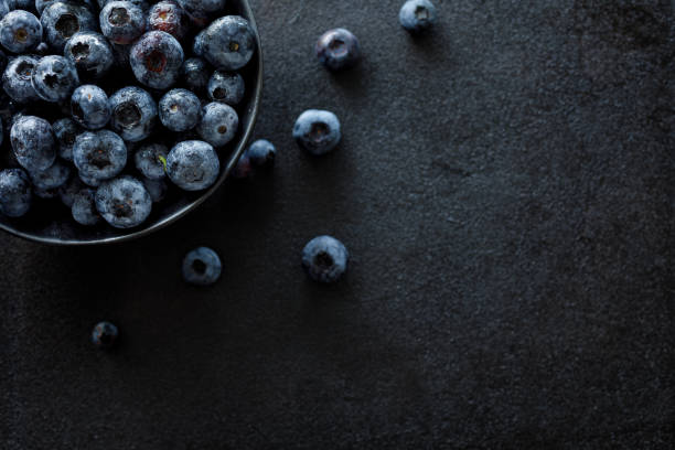istock Fresh blueberries in a dark ceramic bowl on a black background, top view 1164917596