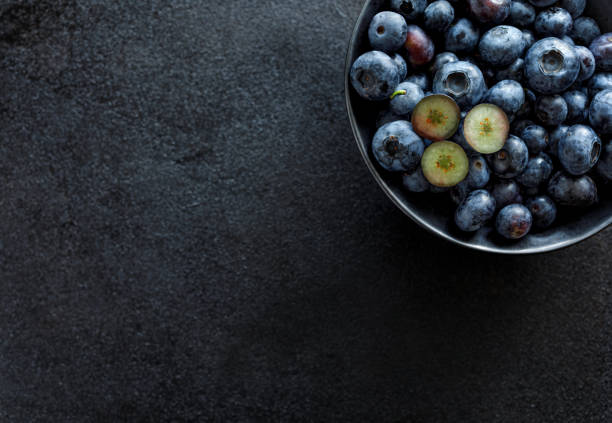 istock Fresh blueberries in a dark ceramic bowl on a black background, top view 1164919529
