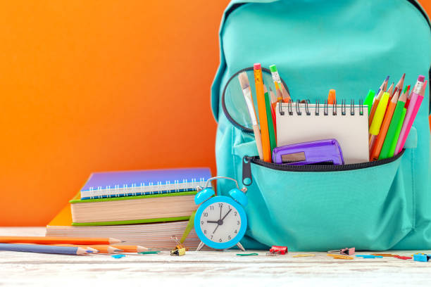 istock Back to School concept. School Backpack with different supplies and alarm clock on orange background 1164922824