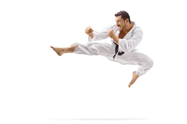 Full length shot of a man performing flying kick in martial arts isolated on white background