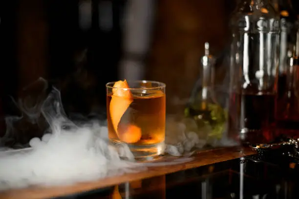 Glass of delicious whiskey with ice cube in steam on bar counter