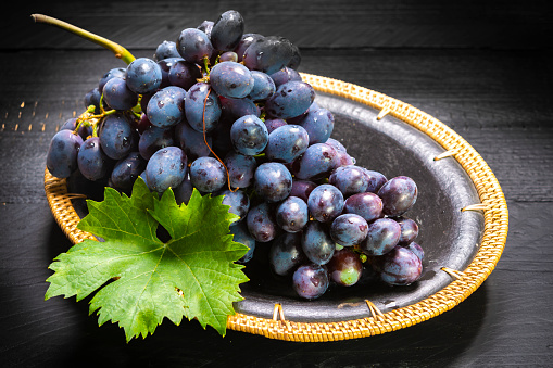 Bunch of ripe blue-black table grapes with leaf served on black plate on black wooden background