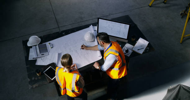 Turning dreams into winning designs High angle shot of two engineers going over a blueprint together in an industrial place of work man in the desk back view stock pictures, royalty-free photos & images