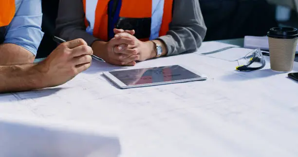Cropped shot of two engineers using a digital tablet while going over a blueprint in an industrial place of work