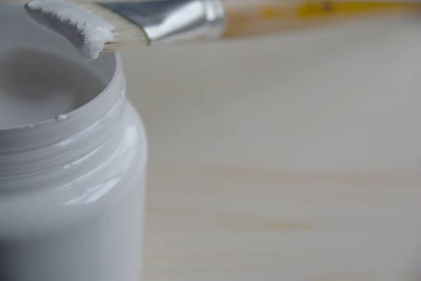 istock Plastic can with white acrylic primer and a bristle brush on a wooden panel. Preparing the surface for drawing. 1164946182
