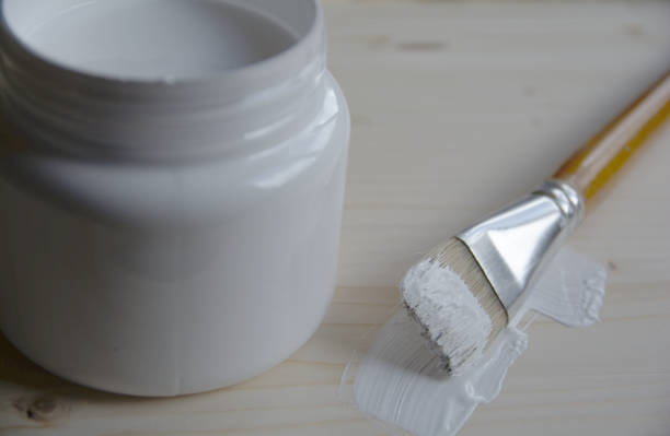istock Plastic can with white acrylic primer and a bristle brush on a wooden panel. Preparing the surface for drawing. 1164946341