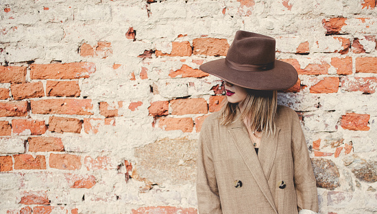 woman in style hat and jacket on brick wall background